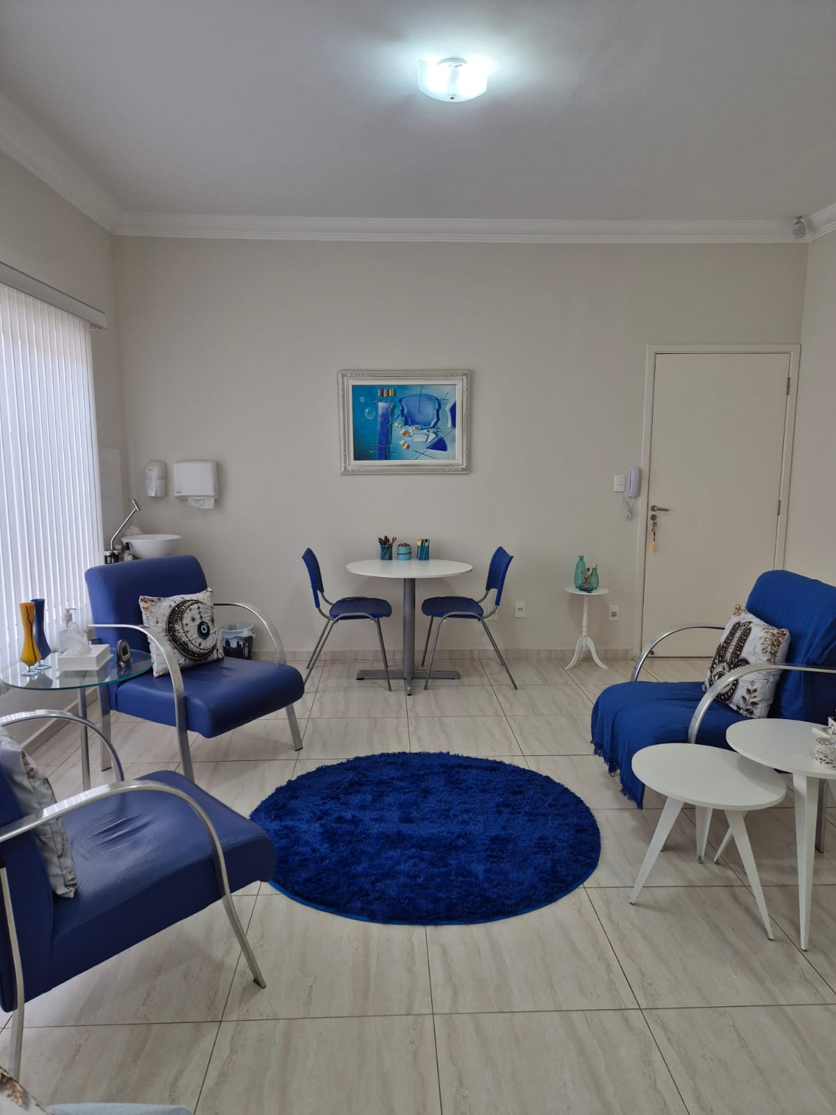 Sala de atendimento com poltronas azuis em roda, tapete redondo azul e mesa ao fundo